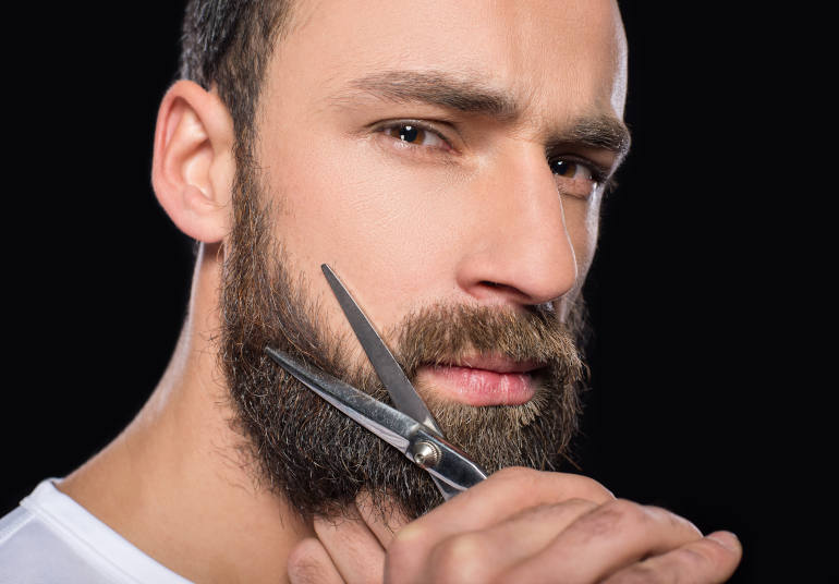 plan sur le visage d’un homme de profil qui taille sa barbe au ciseau après u implant de barbe