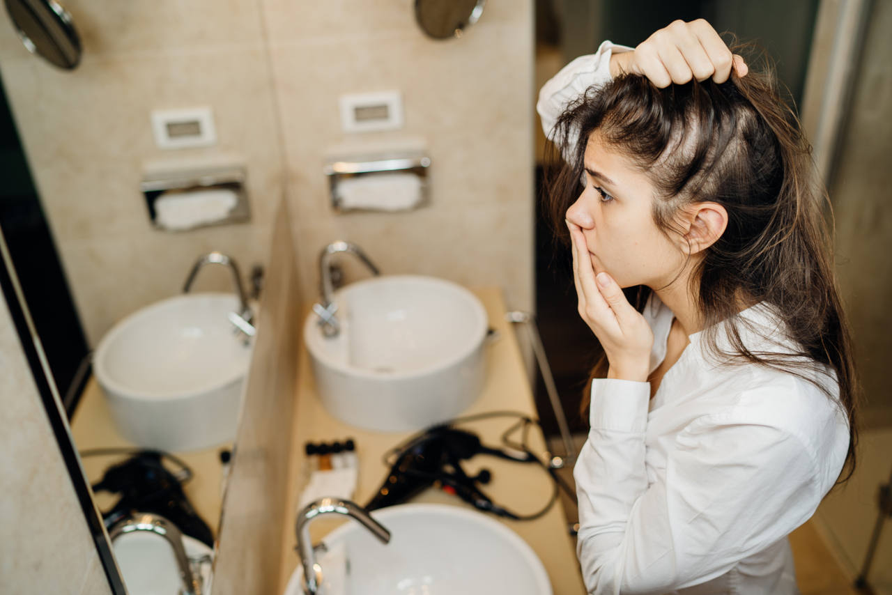 une femme s'inquiète de sa perte de cheveux devant son miroir