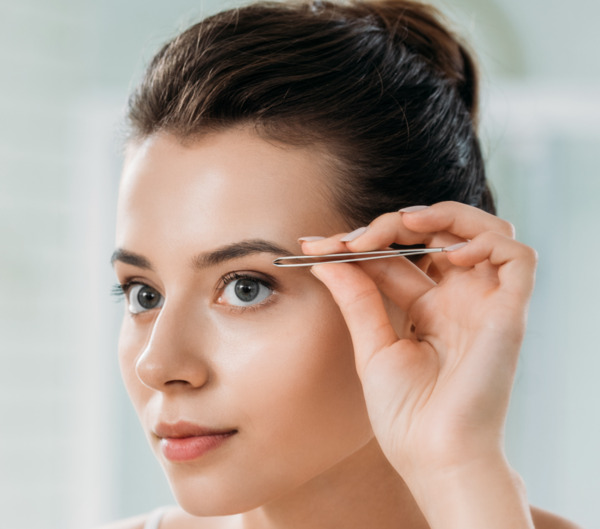 Photo du visage d'une femme aux cheveux châtains s'apprêtant à s'épiler les sourcils avec une pince à épiler