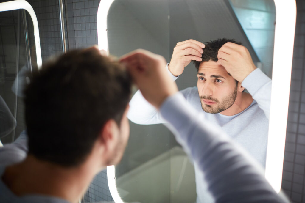 homme en train de regarder sa chute de cheveux devant un miroir
