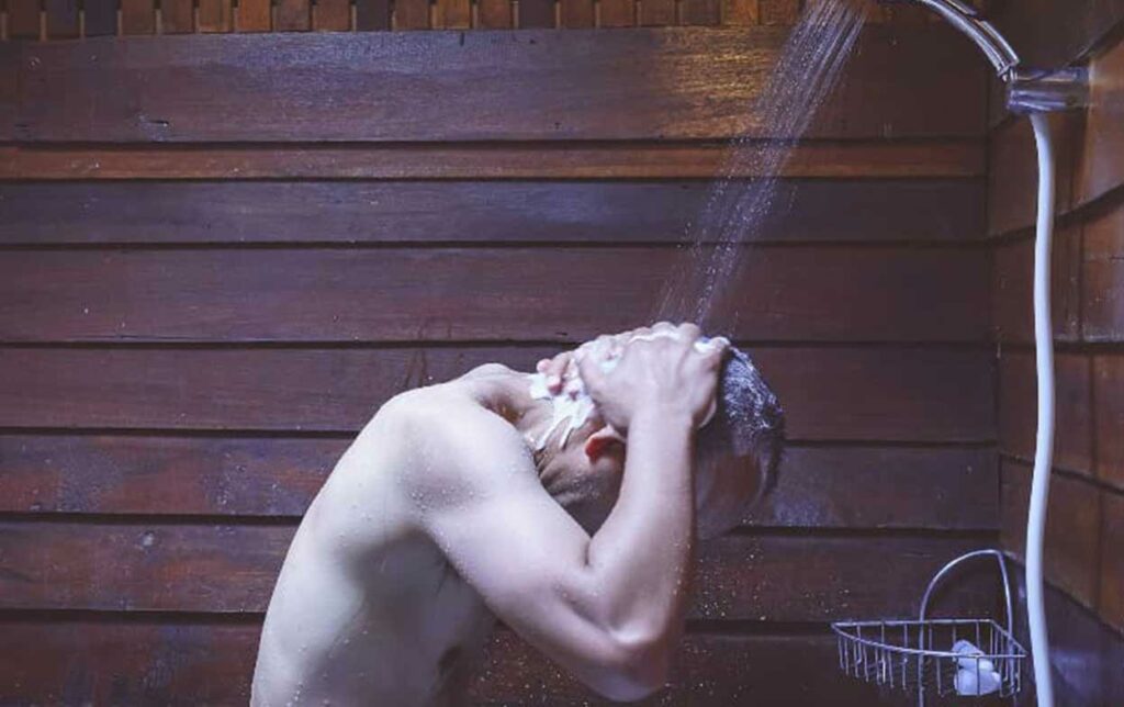 Mann wäscht unter der Dusche die Haare mit Shampoo nach der Haartransplantation