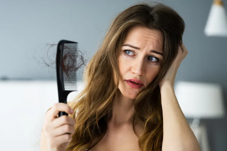 Eine Frau hält einen Kamm, in dem viele Haare sind. Sie ist besorgt um ihren Haarausfall