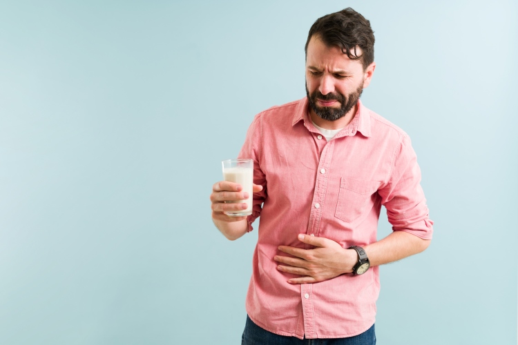 Mann mit einem Glas Milch in der Hand reibt sich den Bauch mit schmerzverzerrtem Gesicht wegen Laktoseintoleranz