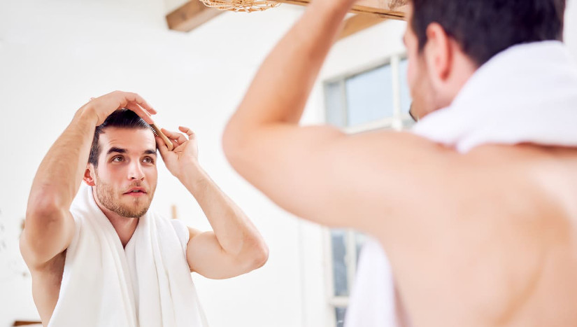 Mann kämmt sich die Haare vor einem Spiegel