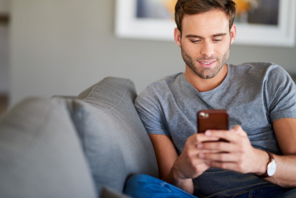 Junger Mann sitzt auf der Couch mit dem Handy in der Hand