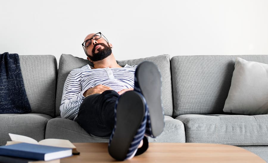 Mann auf der Couch mit Beinen auf dem Tisch.