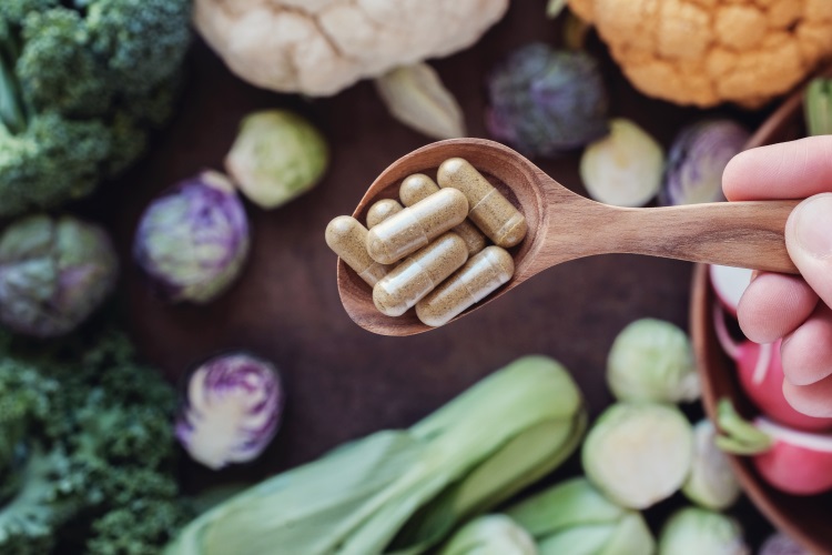 Nahrungsergänzungsmittel auf einem Löffel über einem Tisch mit veganen Lebensmitteln