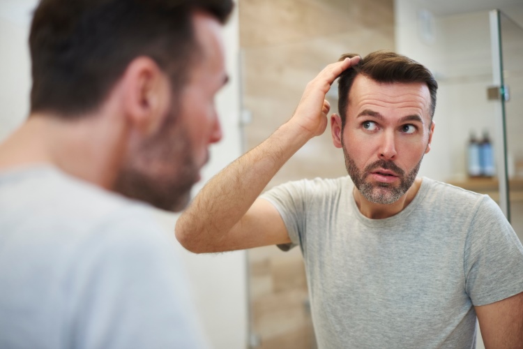 Mann schaut in den Spiegel und betrachtet seinen Haarausfall