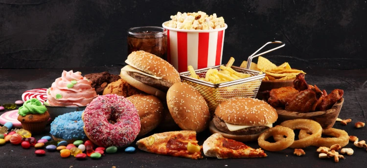 Eine Vielfalt von Fast-Food und Süßigkeiten, darunter Burger, Pizza, Donuts und Pommes, die ungesunde Ernährung und moderne Essgewohnheiten darstellen