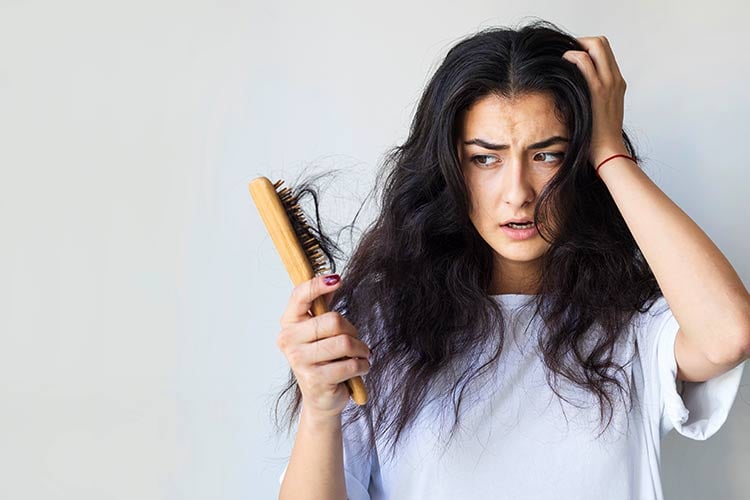 Junge Frau mit besorgtem Gesichtsausdruck, hält eine Bürste mit Haarausfall in der Hand