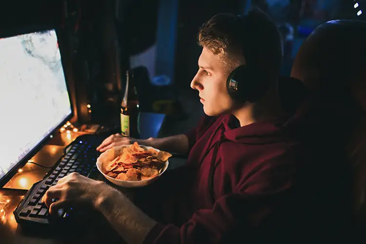 Ein Junger mann sitzt mit einer Schüssel Chips vor dem Bildschirm