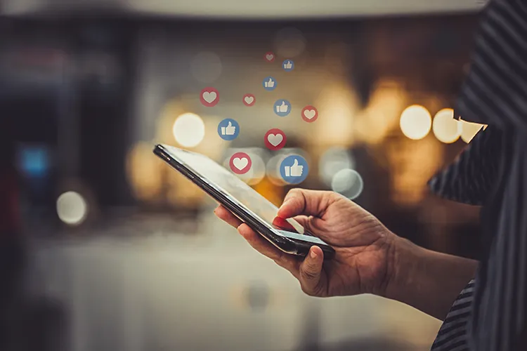 Hand hält ein Smartphone mit eingeblendeten Like- und Herzsymbolen