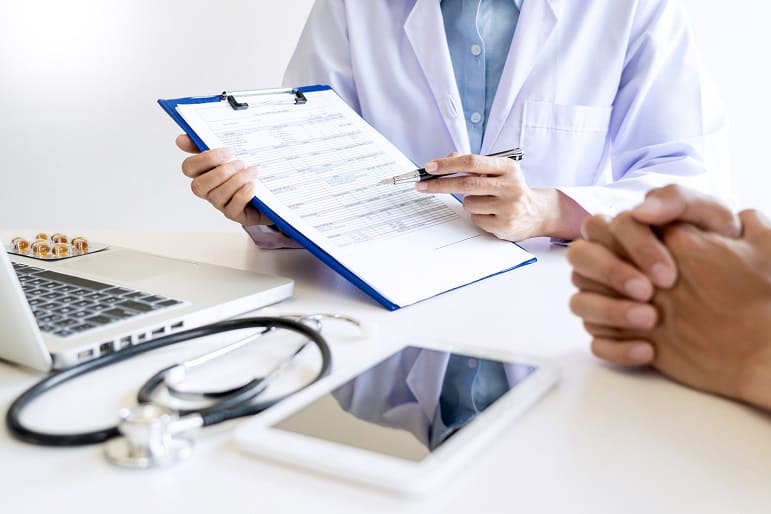 Arzt zeigt vor einem Patienten mit einem Stift auf einen Fragebogen zum Aufüllen