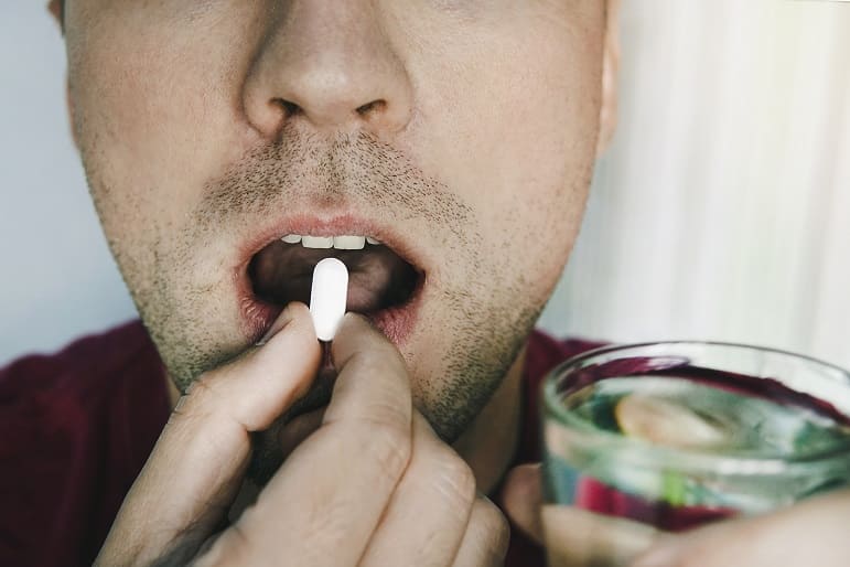 Mann mit offenem Mund schluckt eine Pille mit einem Glas Wasser in der Hand