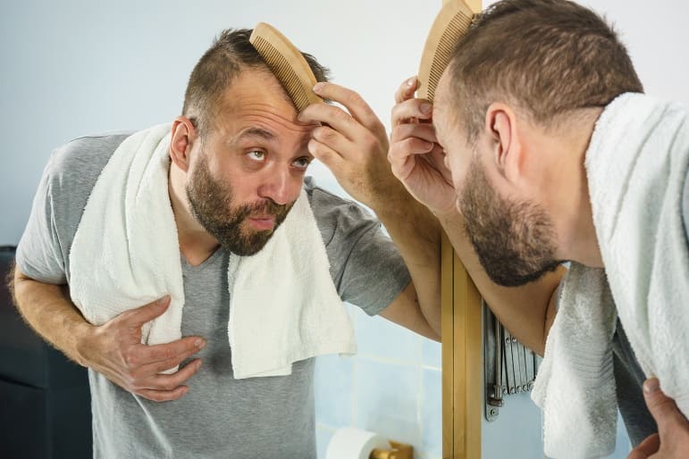 Mann steht vor dem Spiegel und kämmt seine dünnen Haare
