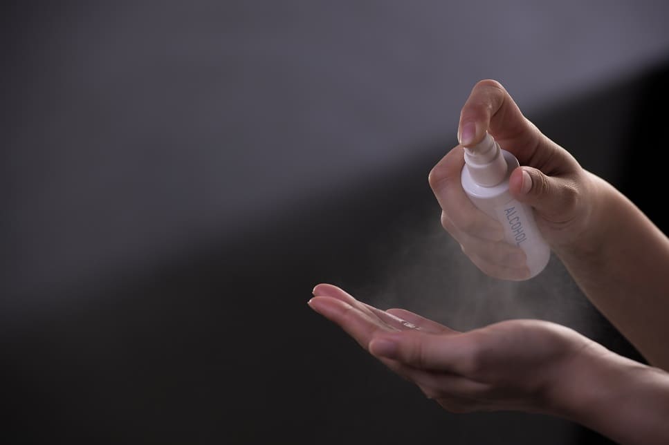 Frau besprüht ihre Hände mit Desinfektionsspray