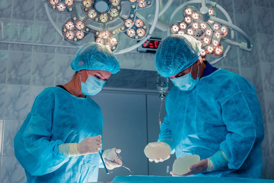 Ärte im Operationssaal bei der OP mit Silikonimplantaten in der Hand