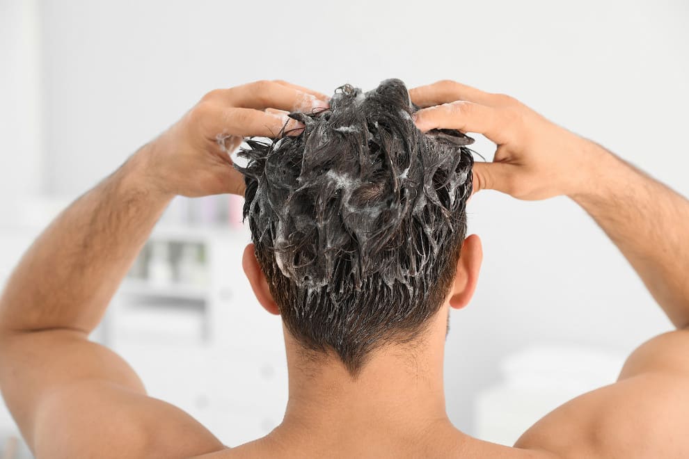 Mann massiert sich im Badezimmer Shampoo in die Haare