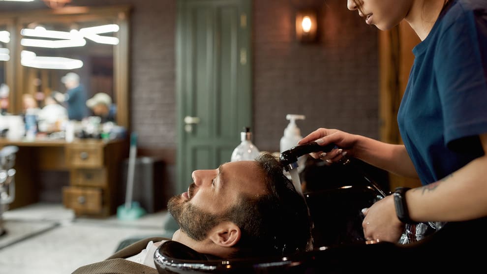 Mann beim Friseur Haare waschen verliert Haare als Anzeichen für Haarverlust