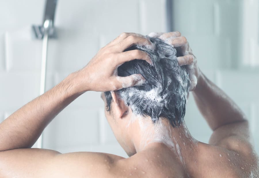 foto di un uomo che utilizza uno shampoo a base di caffeina per capelli