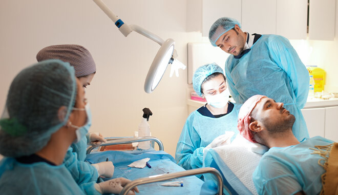 A imagem mostra o Dr. Balwi a supervisionar a sua equipa médica durante um transplante capilar num doente.