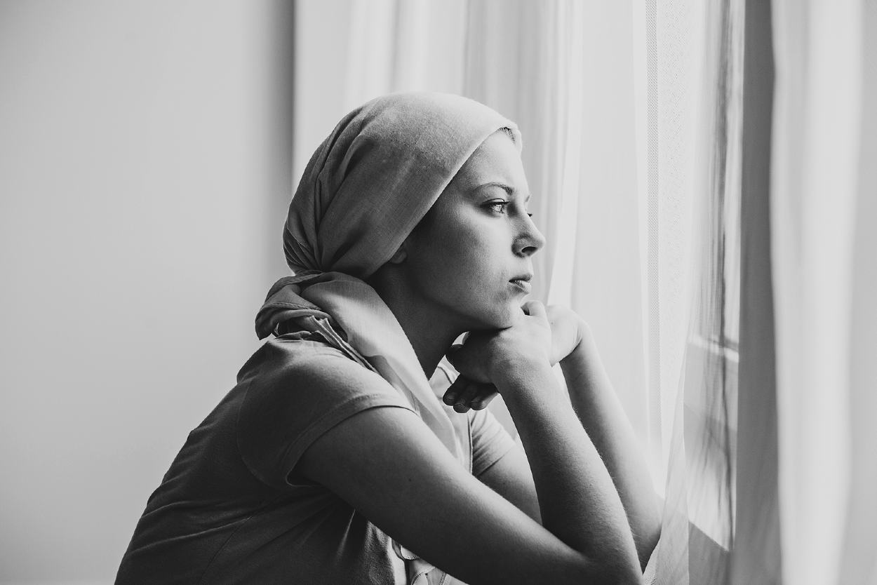 Mujer con un pañuelo en la cabeza mirando por la ventana
