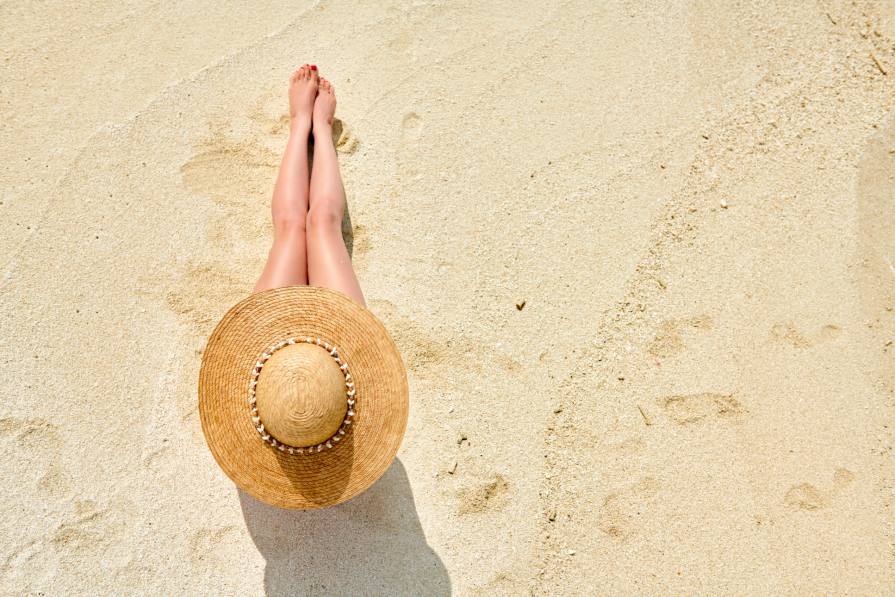Mujer sentada en la playa con sombrero de paja