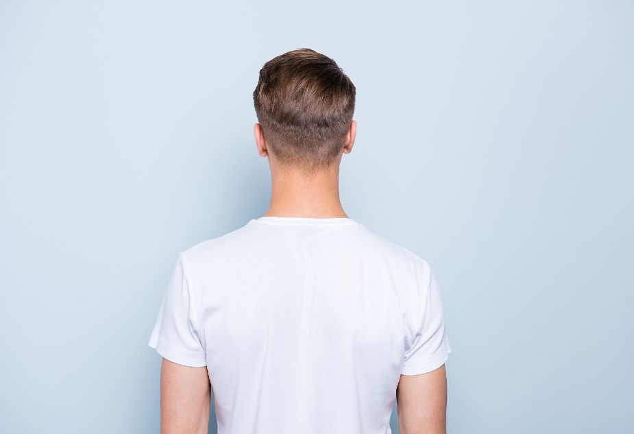 Hombre de espaldas a la cámara con camiseta blanca y cabello crecido tras el injerto capilar.