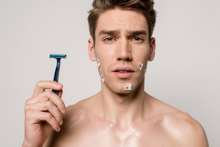 Hombre sujetando cuchilla de afeitar con cortes en el rostro