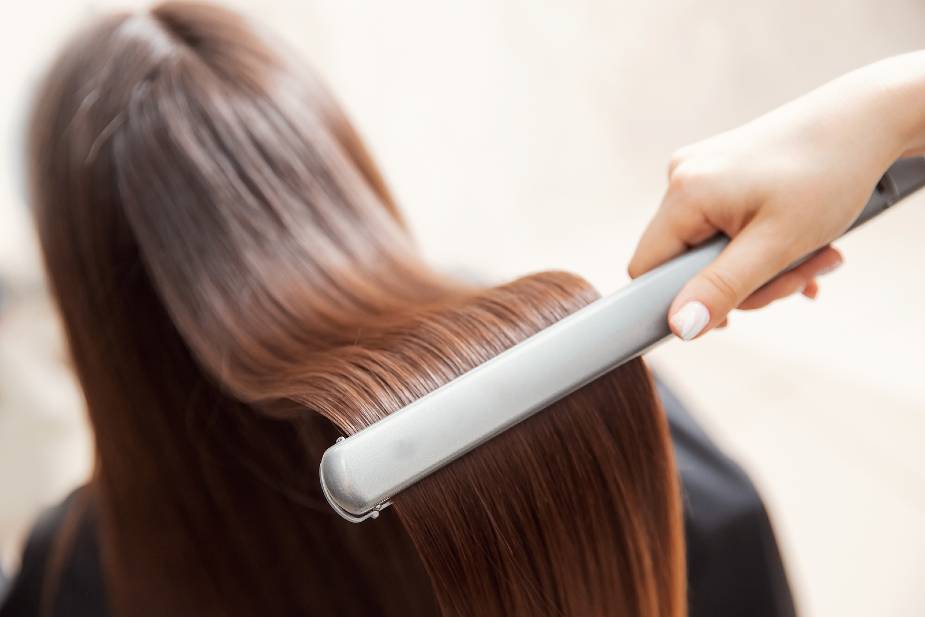 Mujer alisándose el pelo con un alisador tras un tratamiento de keratina