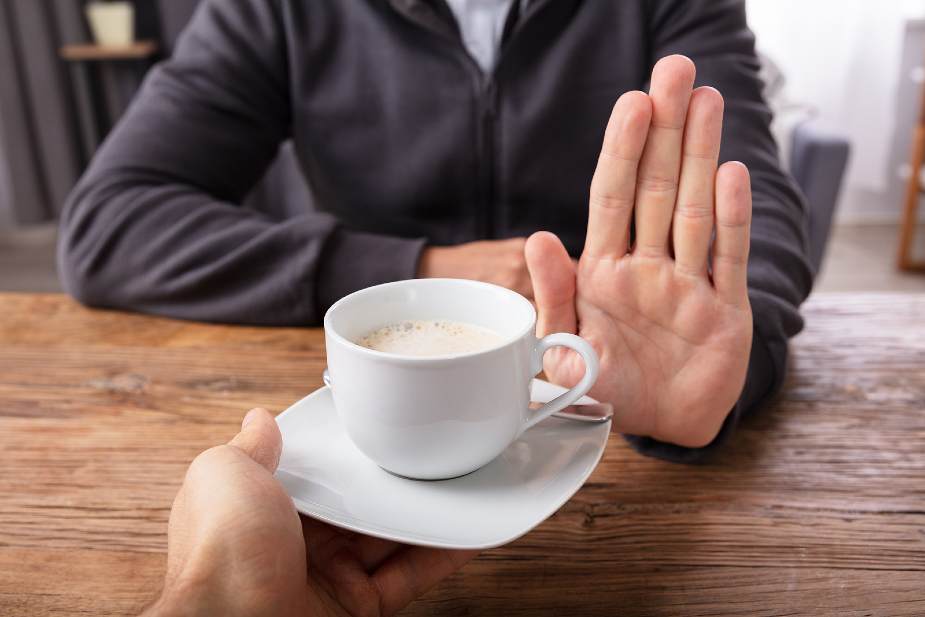 Hombre renunciando a una taza de café con la mano durante el preoperatorio del injerto capilar.