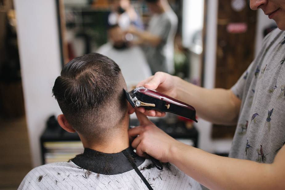 Hombre cortando el pelo a un cliente con maquinilla.